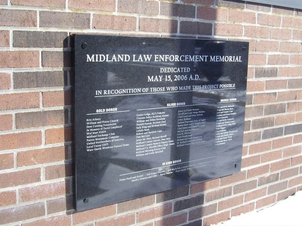 Black memorial plaque on a brick wall dedicated to the Midland Law Enforcement Memorial, dated May 15, 2006, recognizing donors and contributors.