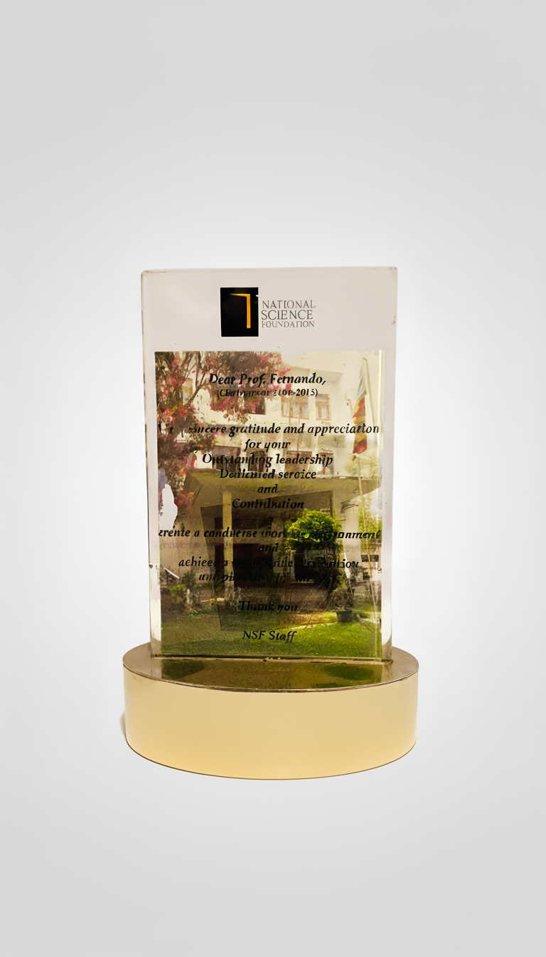 A clear glass award with etched text and the logo of the National Science Foundation, mounted on a round, beige base, with a reflection of a house and trees on the glass surface.