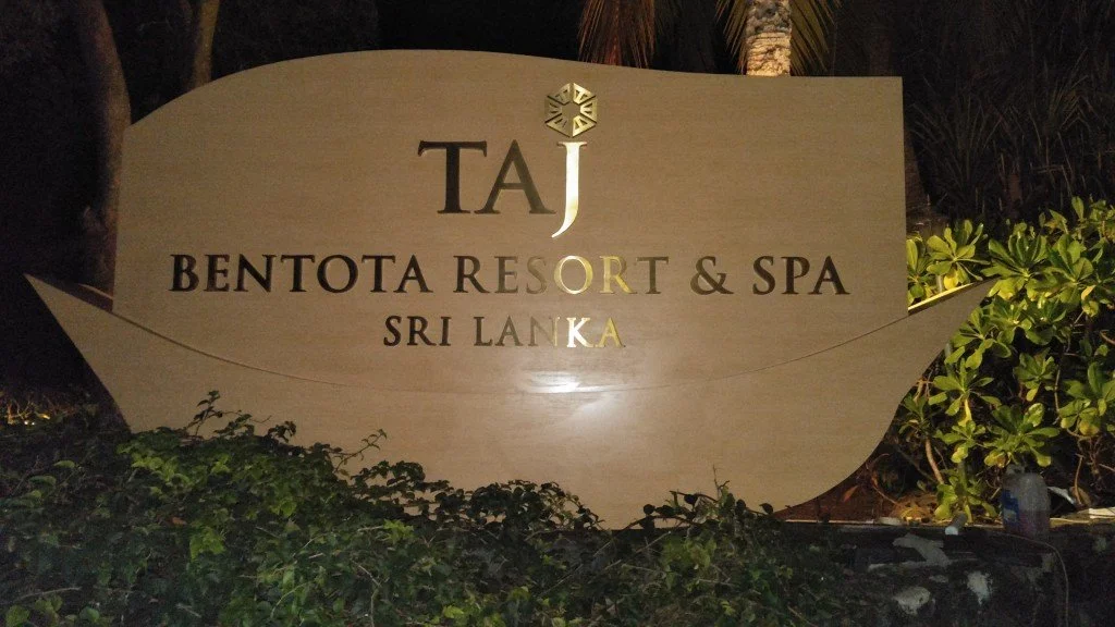 Sign for Taj Bentota Resort & Spa in Sri Lanka illuminated at night, surrounded by greenery.