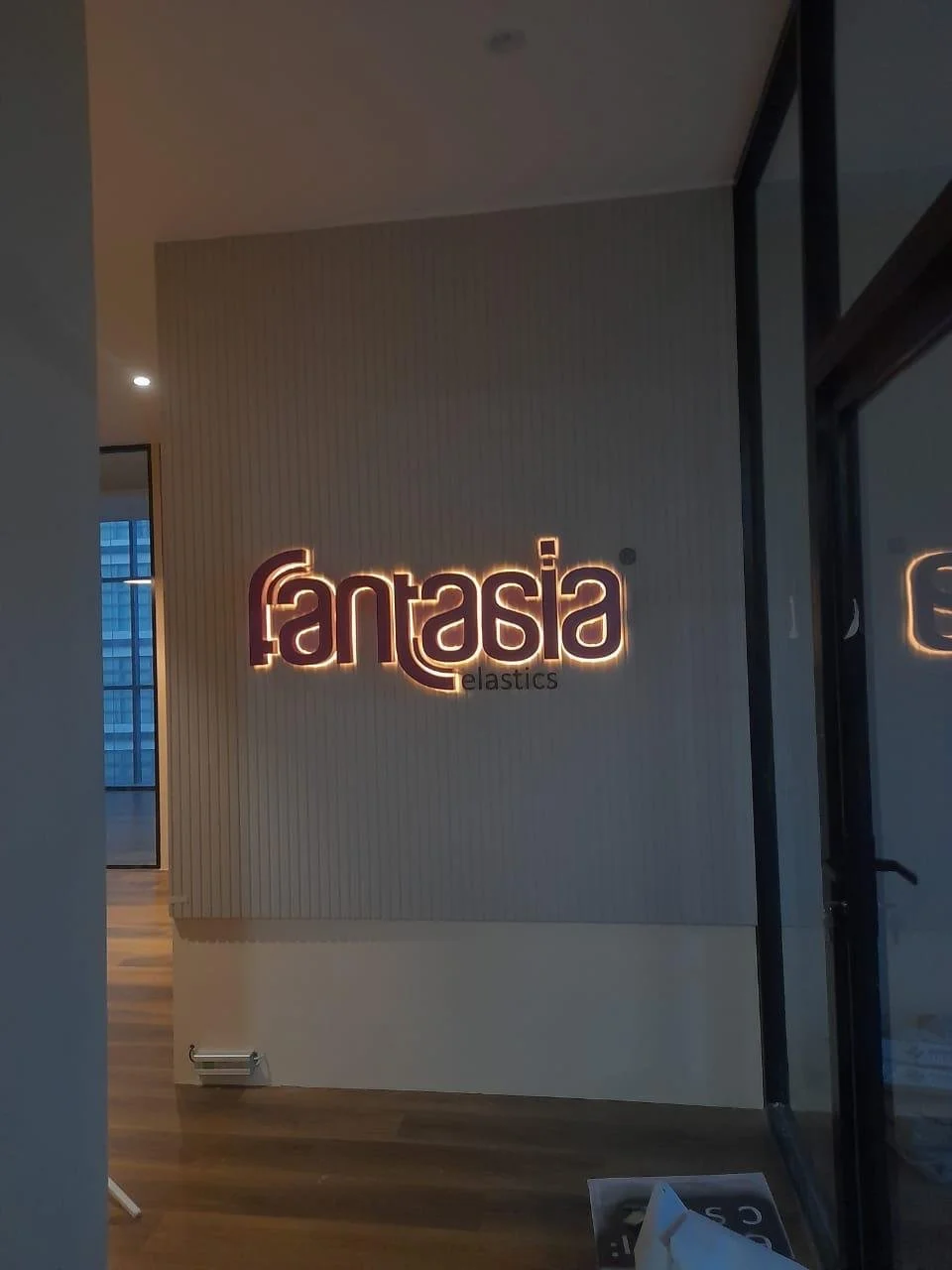 Interior view of a building with a illuminated sign on the wall that reads 'fantasia elastics'.