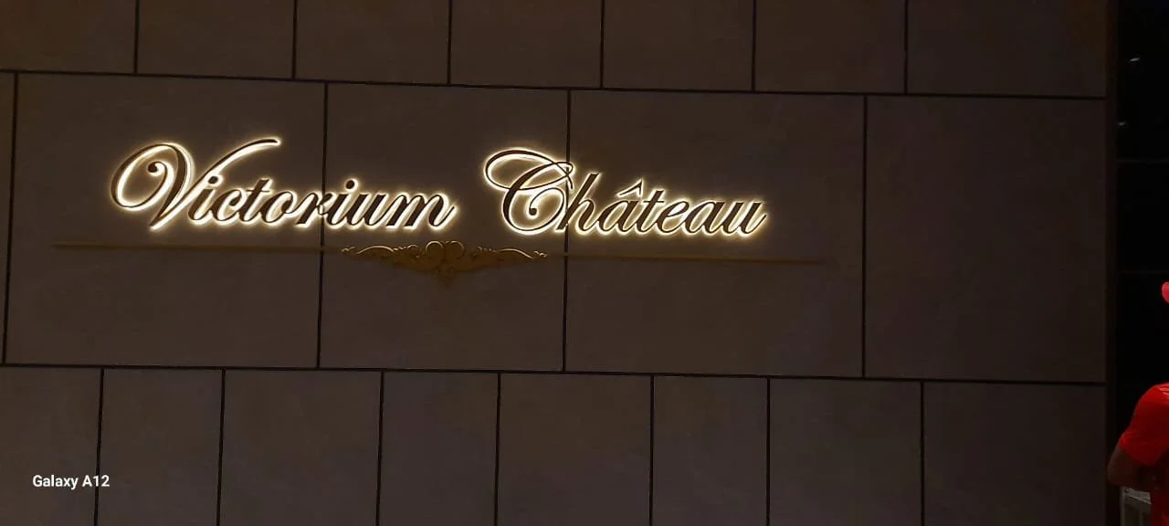 Illuminated sign on a wall reads  a0Victorum Chateau a0 in elegant cursive font.