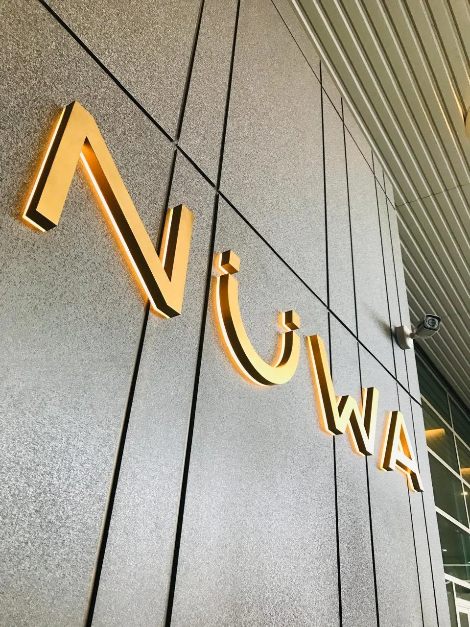 Close-up of a sign with the text 'NI' in illuminated 3D letters mounted on a gray tiled wall.