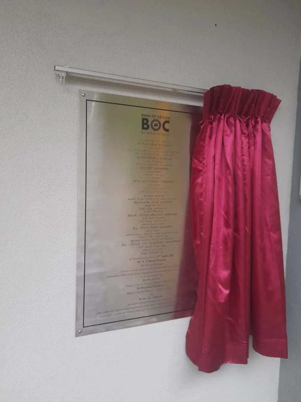 A plaque on a white wall with a pink curtain partially covering it.