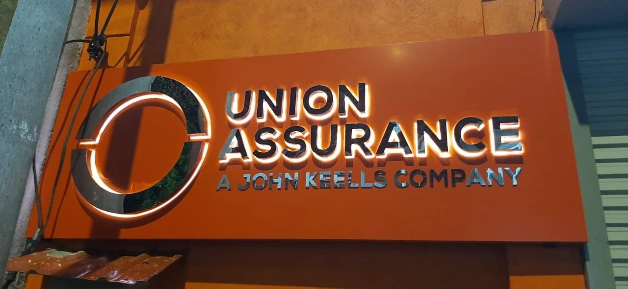 Illuminated sign on a building with the text "Union Assurance a John Keells Company" and a circular logo to the left.