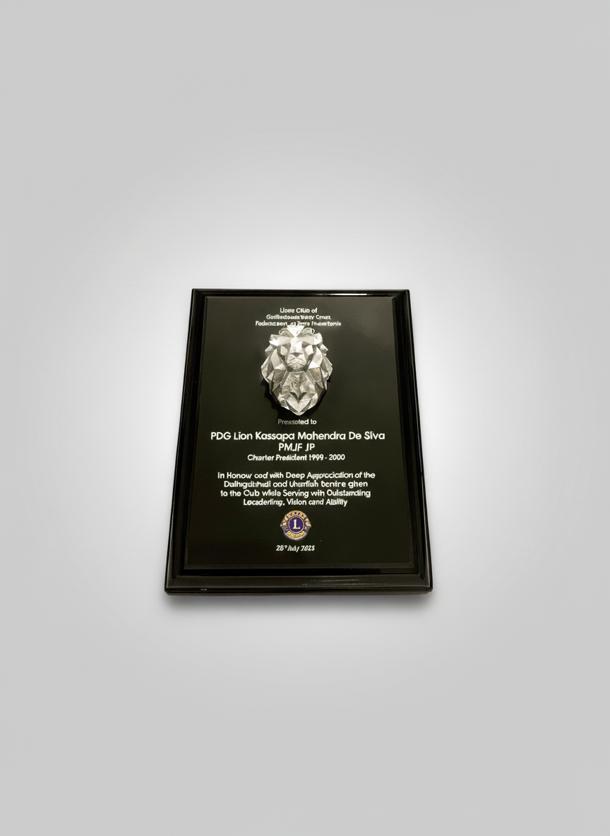 A black-framed plaque with a lion's head sculpture at the top and text in white, honoring PDG Lion Kassapa Mahendra De Silva, presented by the United Club of Gothaboonda County Chemet, on July 26, 2023.