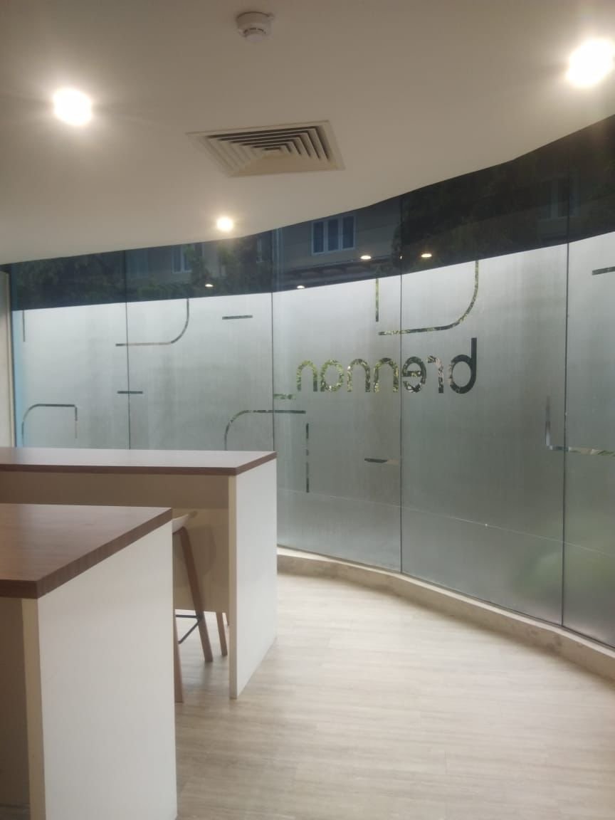 An office space with a curved glass wall, a white counter, a chair, and overhead lighting.
