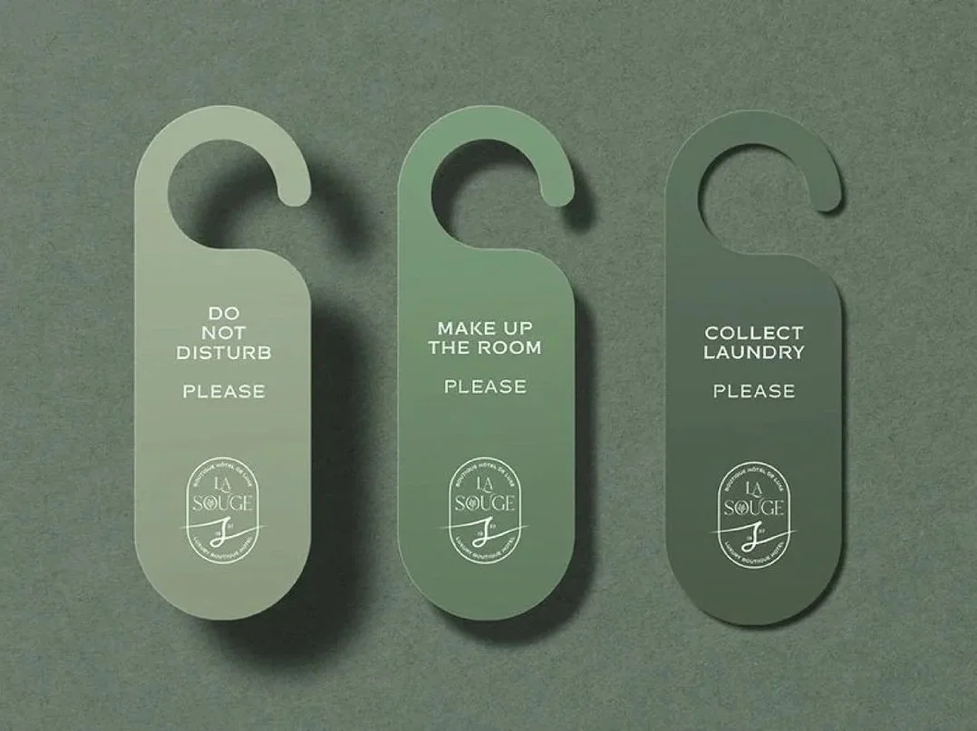 Three green door hangers with white text and logo, reading "Do Not Disturb Please", "Make Up The Room Please", and "Collect Laundry Please" on a gray background.