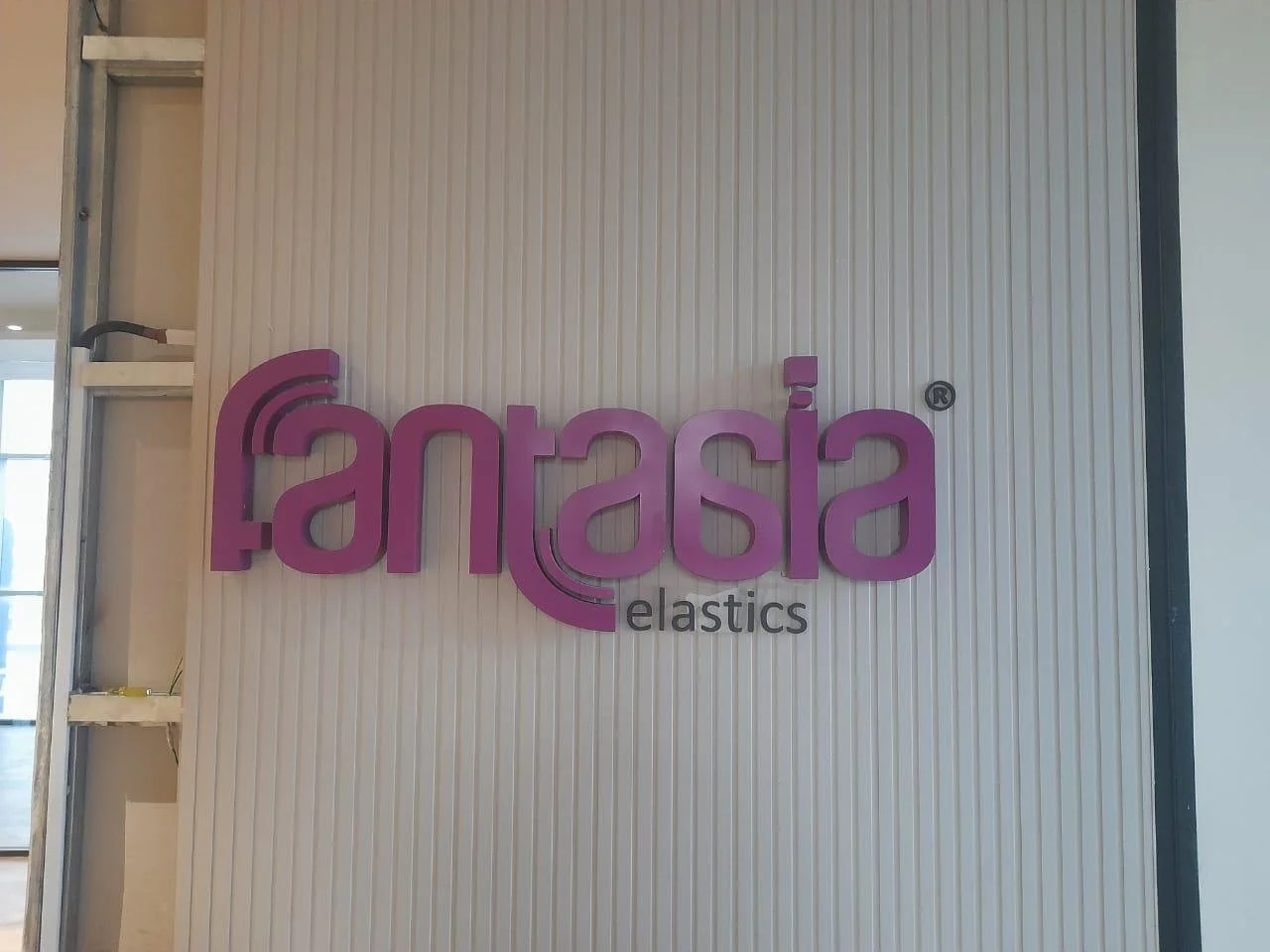 Sign reading 'fantasia elastics' in purple letters on a white wall.
