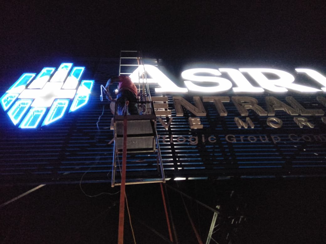 A worker on a scaffold installing or repairing illuminated signage on the exterior of a building at night. The sign reads 'EASTSIDE' and includes a logo.