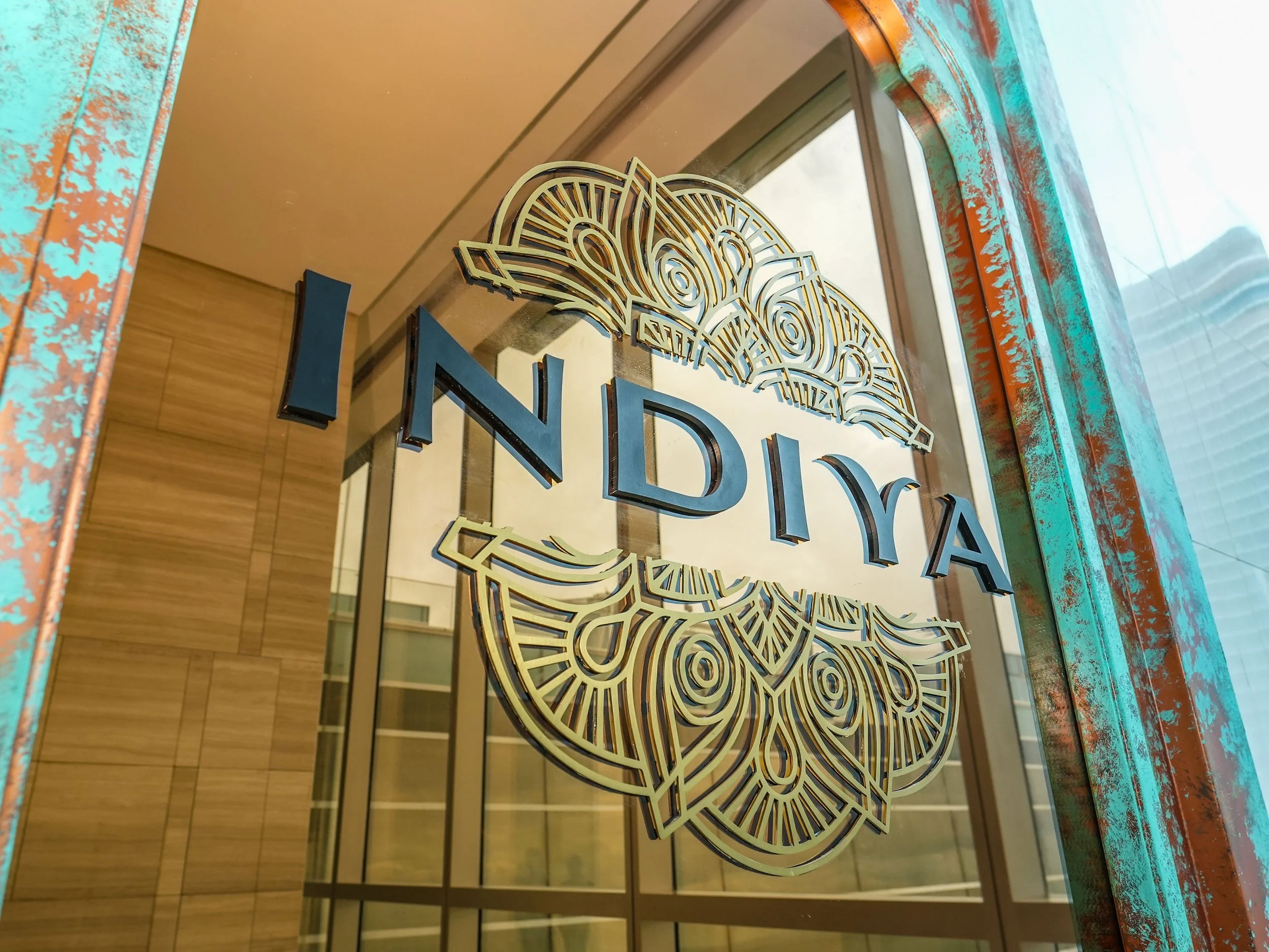 Decorative sign with gold accents and the word 'INDIA' in bold letters, reflected on a glass surface with a wood-paneled wall in the background.