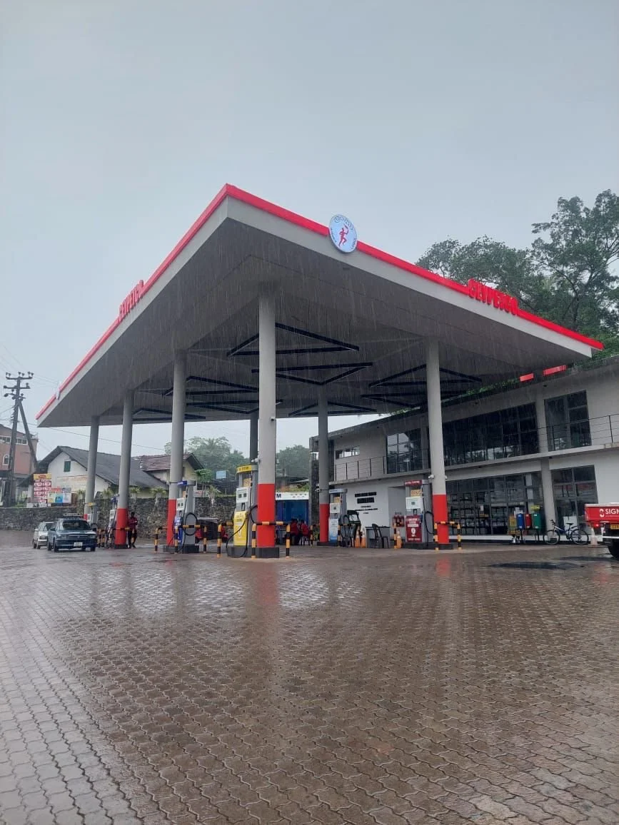 Gas station with multiple fuel pumps, a convenience store, and a car parked while refueling on a rainy day.