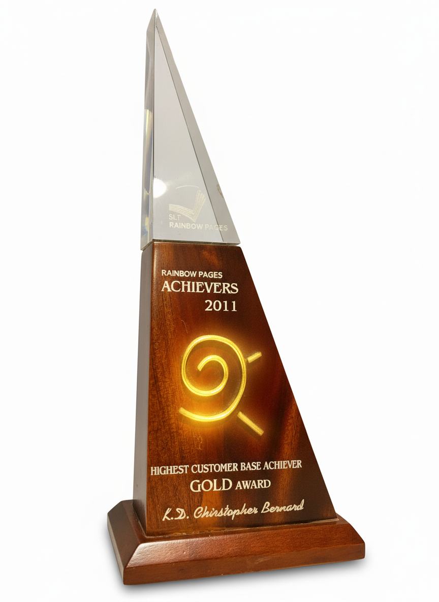A tall wooden and glass award trophy with the inscription 'Rainbow Pages Achievers 2011, Highest Customer Base Achiever Gold Award, K.D. Christopher Bernard'.