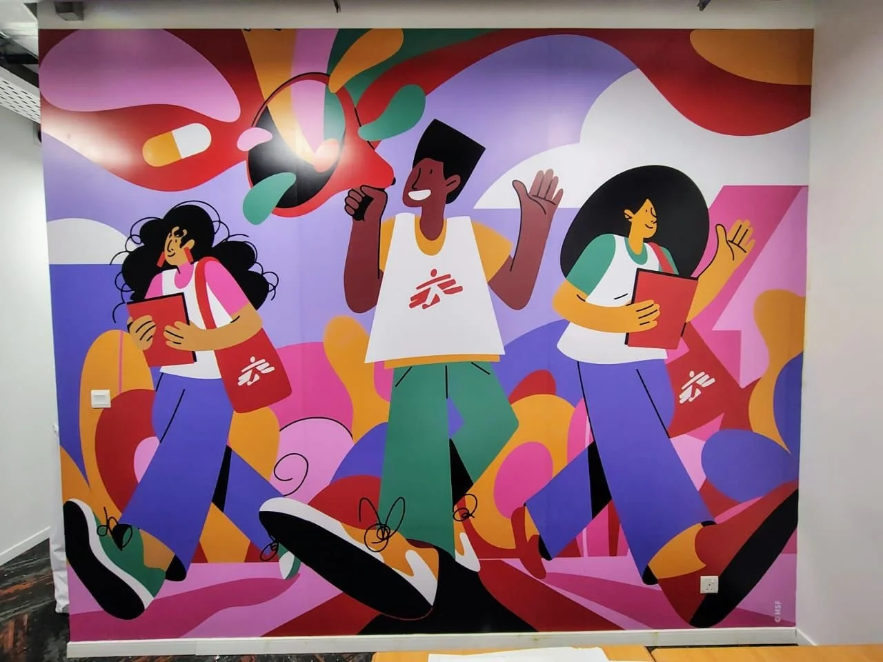 Colorful mural of three animated people walking, carrying books and bags, surrounded by vibrant abstract shapes and patterns.