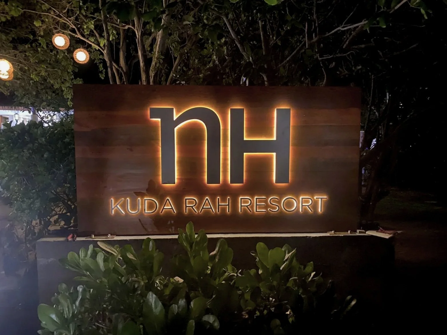 Illuminated sign for Kuda Rah Resort at night, with large 'KH' letters and smaller text beneath it.