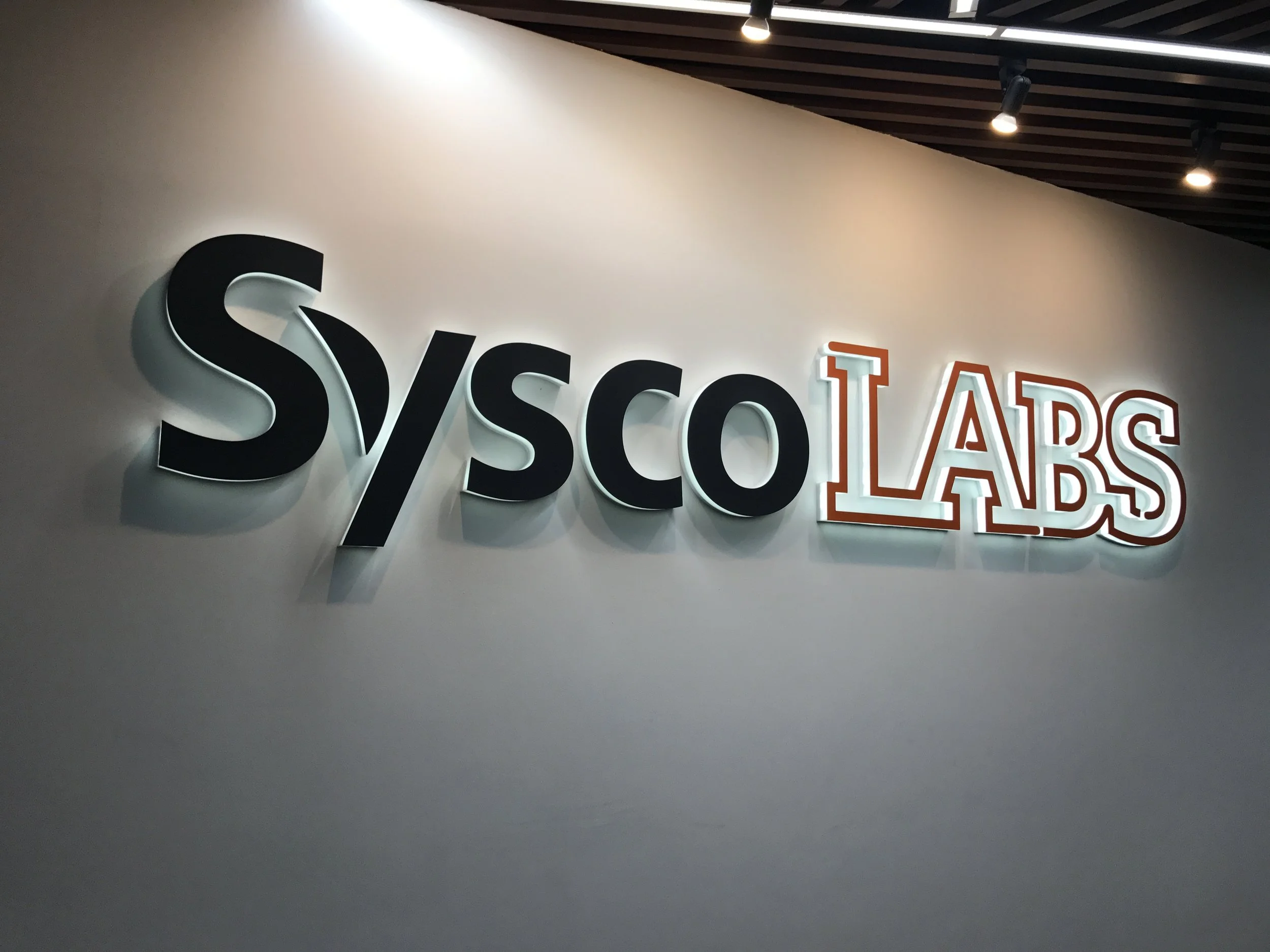Close-up of illuminated 3D sign reading 'SVSOC' on a white wall with a partial view of the word 'LABS' in orange outline.