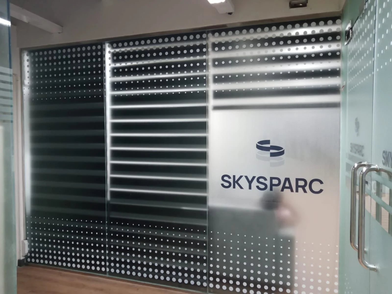 Glass doors with dotted pattern, with a logo and text that reads 'SKYSPARC' on the right door, located inside a modern building.