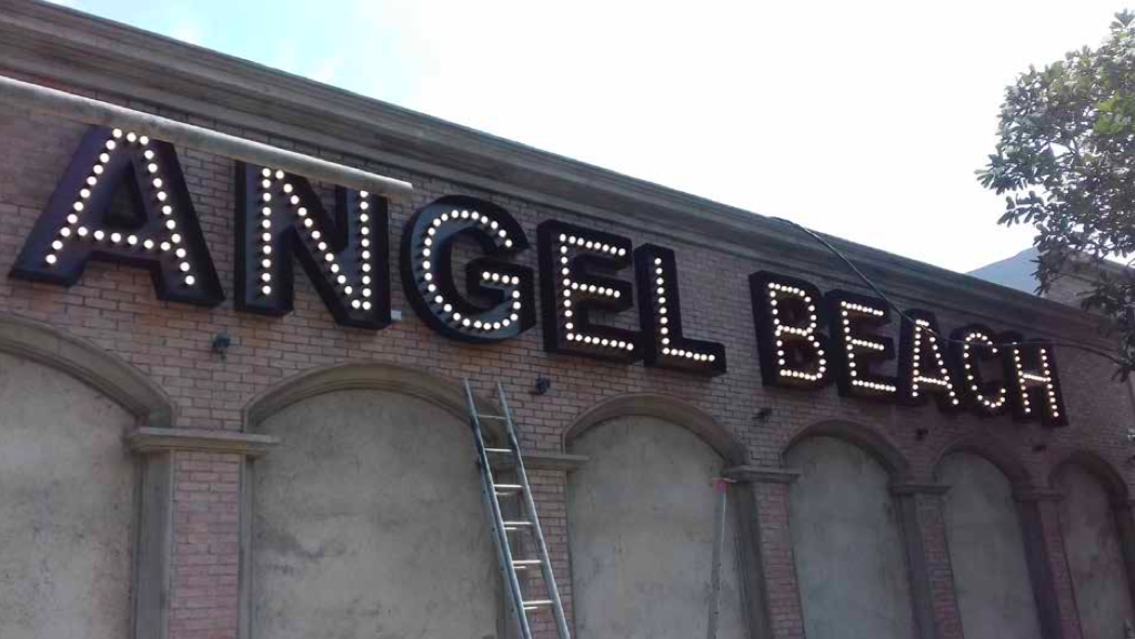 Close-up of a brick building with a lit-up sign that reads 'ANGEL BEACH' in large capital letters.