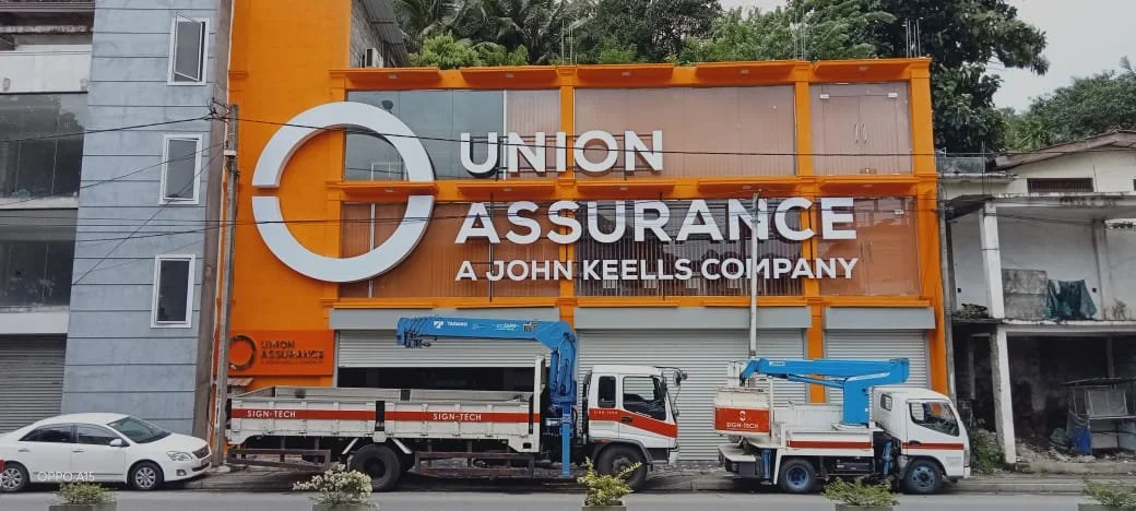 Orange building with a large sign reading 'Union Assurance, A John Keells Company,' and two trucks parked in front.