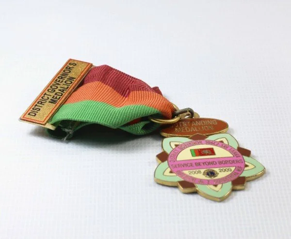 A multicolored veteran's service medal with a green, orange, and red ribbon and several attached pins, including one labeled "District Governors Megalon" and another with the text "Service Beyond Borders 2008-2009."