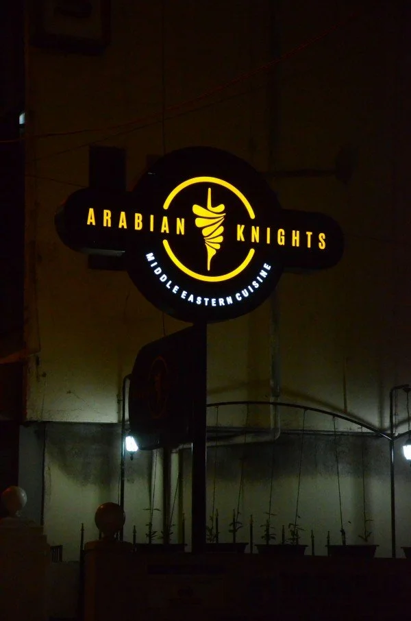 Neon sign for Arabian Knights Middle Eastern cuisine restaurant at night, featuring a sword wrapped with a cloth in the logo.