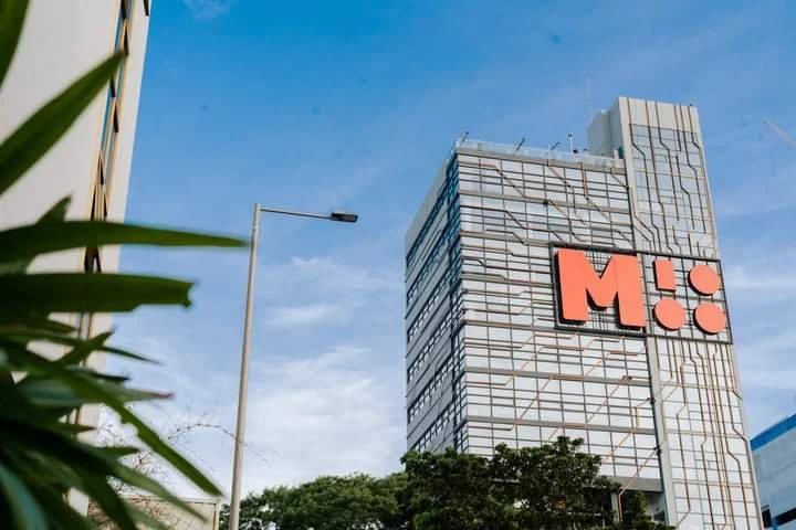 Tall office building with a large red logo on the facade and a blue sky background.
