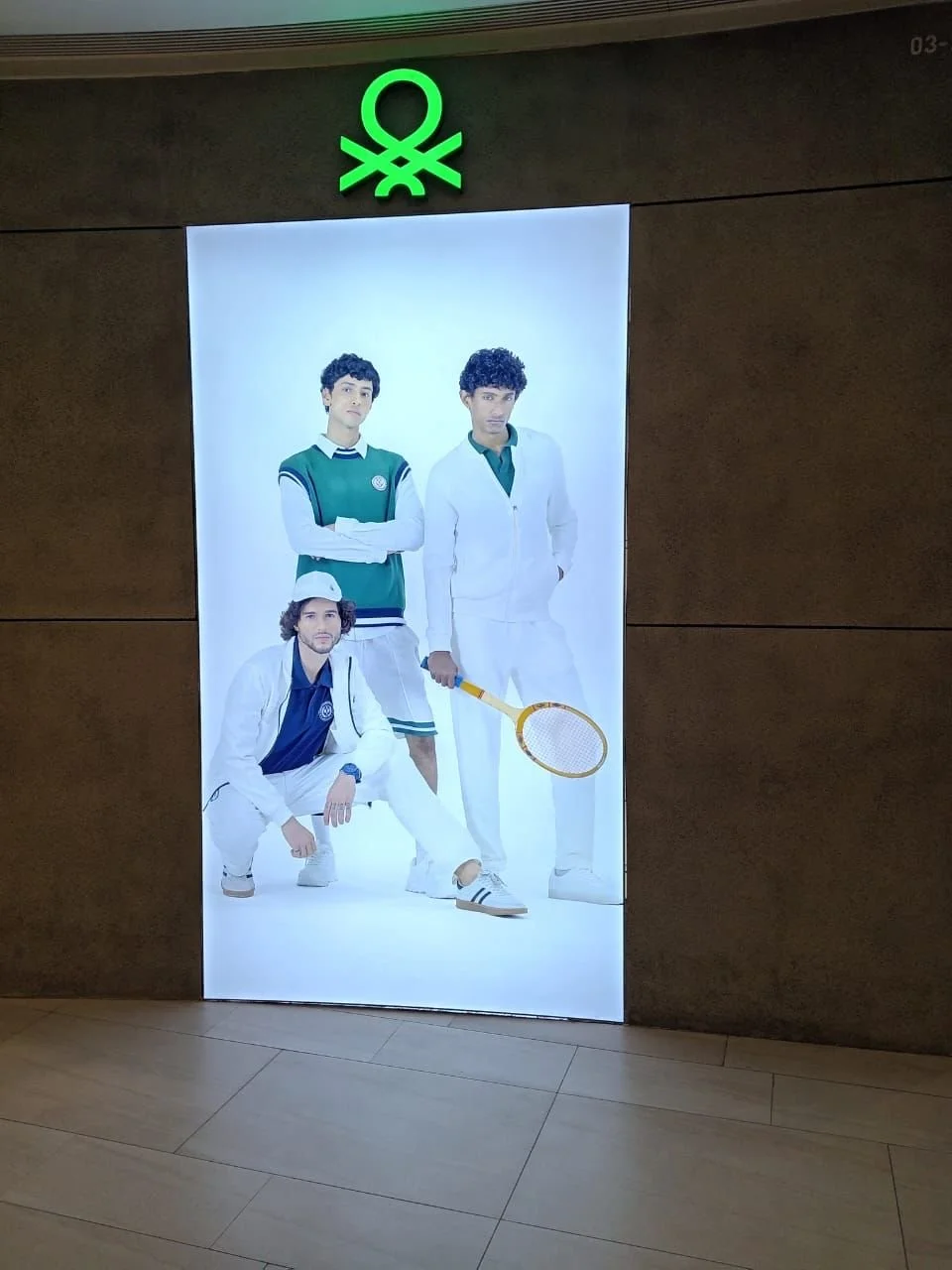 An advertisement poster featuring four young men dressed in tennis or sportswear, standing and crouching against a white background. One holds a tennis racket, and they pose confidently.