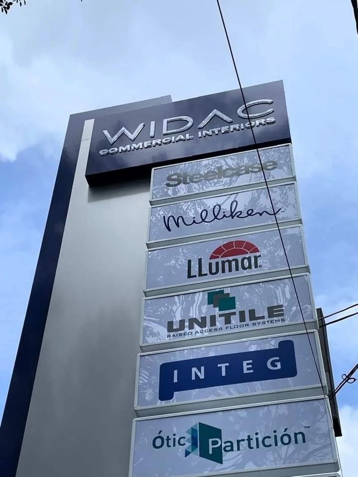Sign for WIDA Commercial Interiors with logos of various companies, including Steelcase, Milliken, LLumar, UNtILE, INTEG, and Ótic Partición.