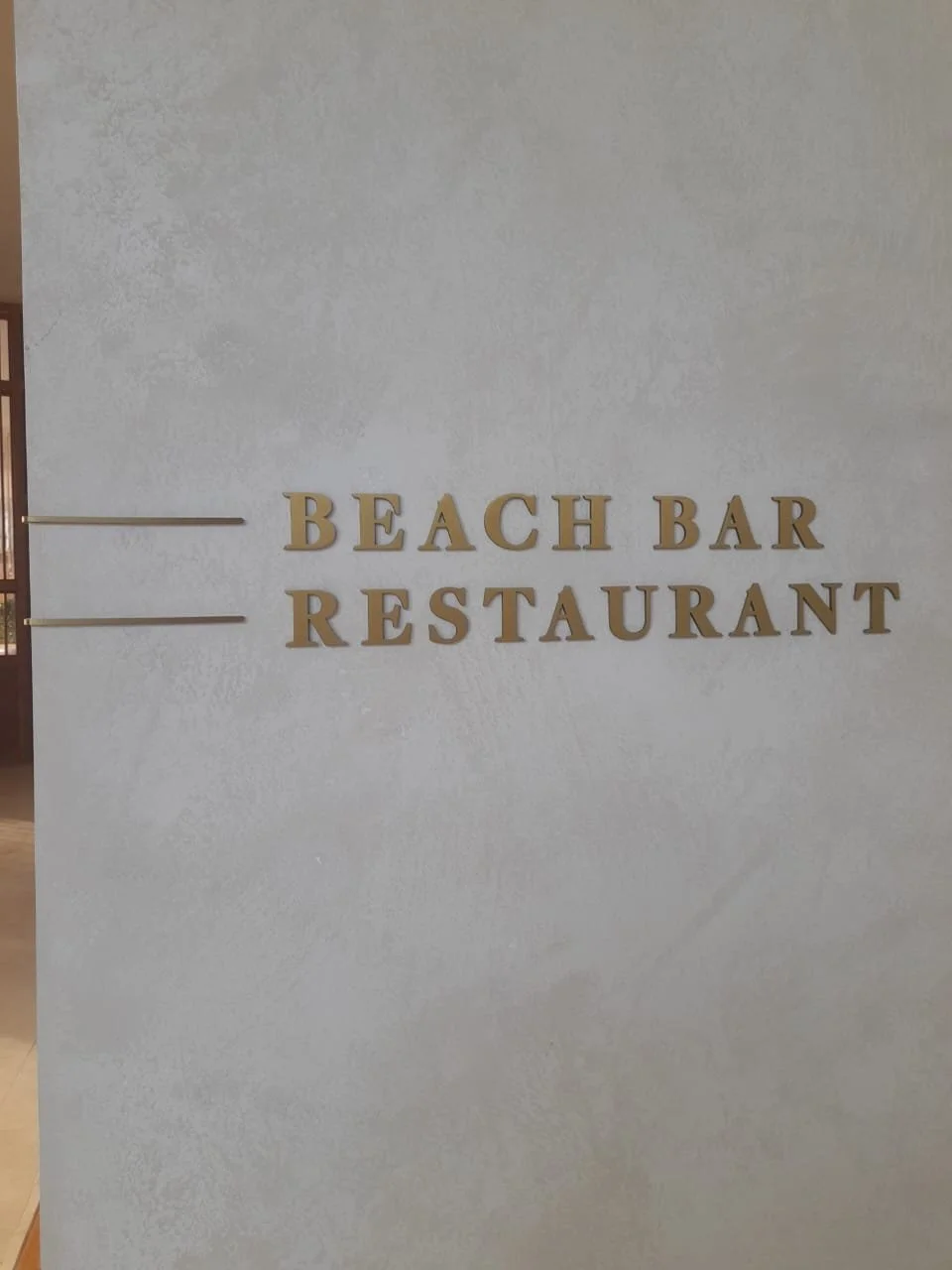 Sign on a wall with gold letters reading "Beach Bar Restaurant".