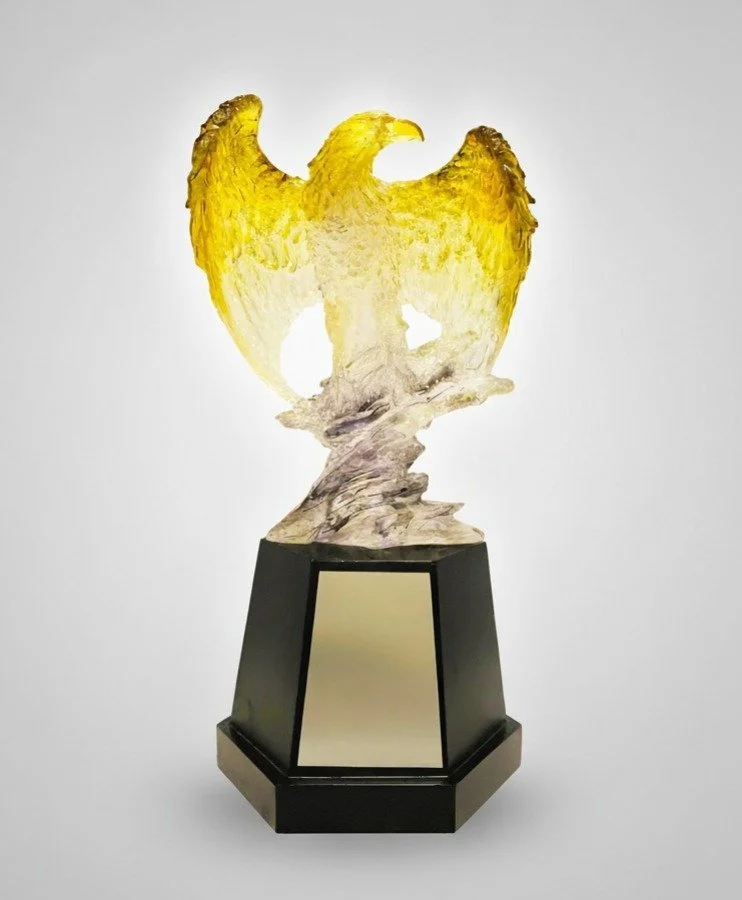 Glass sculpture of a bald eagle with yellow wings on a black base.