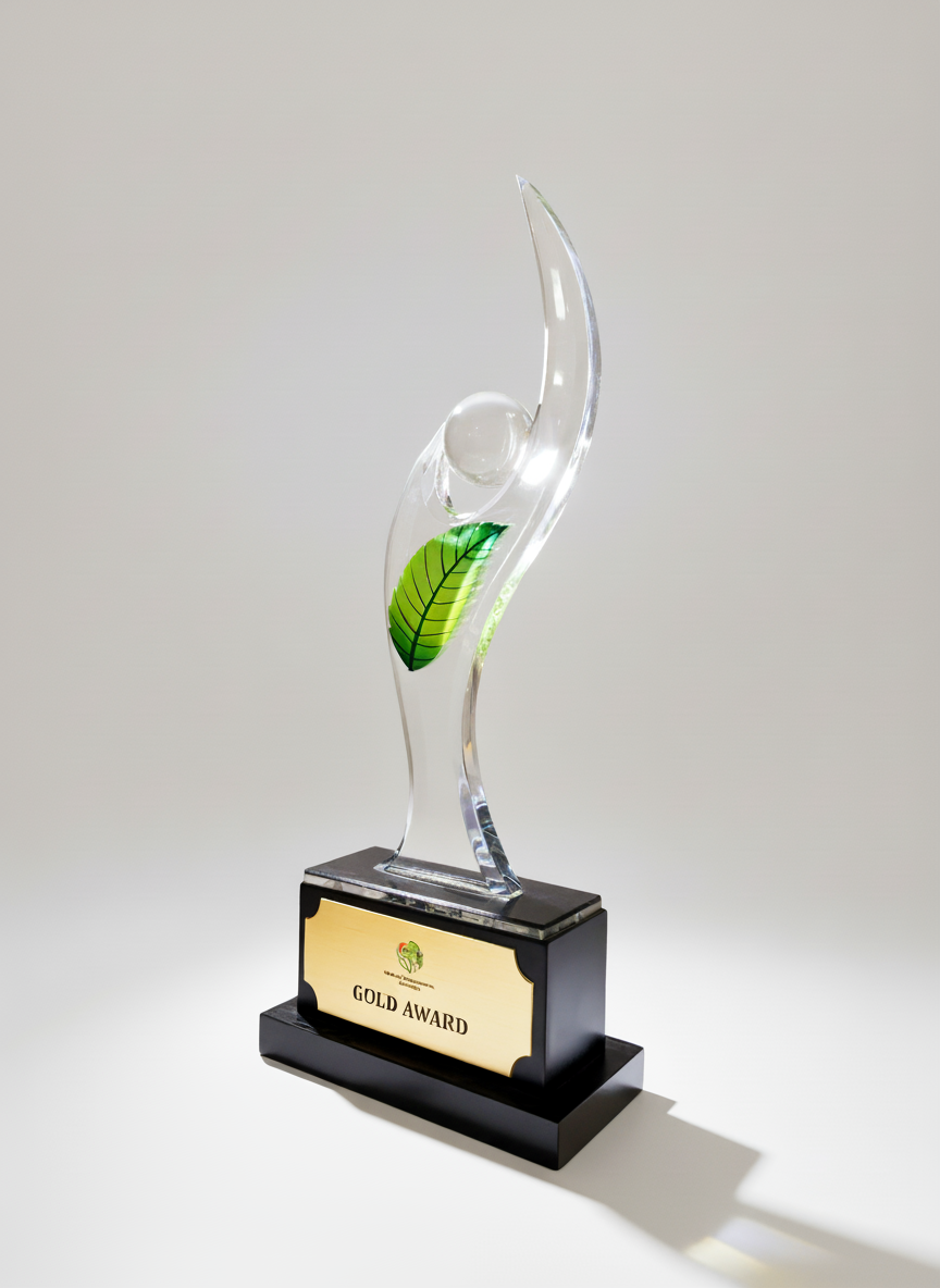 A trophy with a clear, curved glass figure featuring a green leaf design and a white spherical element, mounted on a black base with a gold-colored plaque labeled 'GOLD AWARD'.