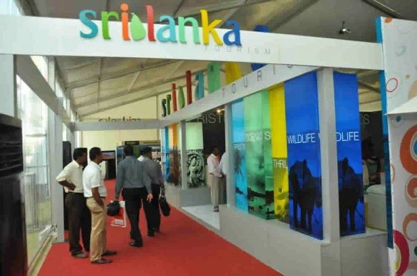 Trade show booth with 'Sri Lanka' colorful sign and wildlife-themed displays, with several people walking and talking.