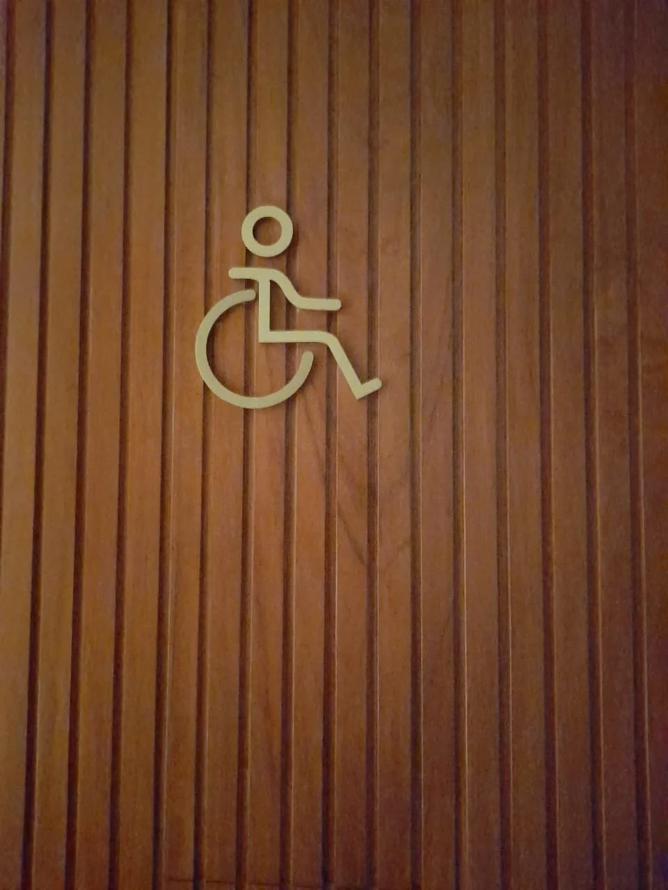Accessibility sign for a wheelchair accessible facility on a wood-paneled wall.