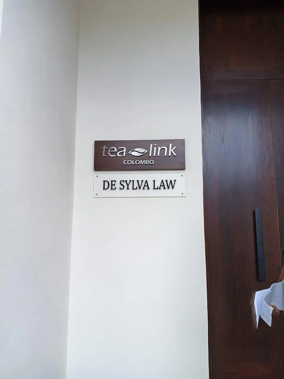 Interior wall with two business signs: one for Tea Link Colombo and another for De Sylva Law, with a dark wooden door on the right side.