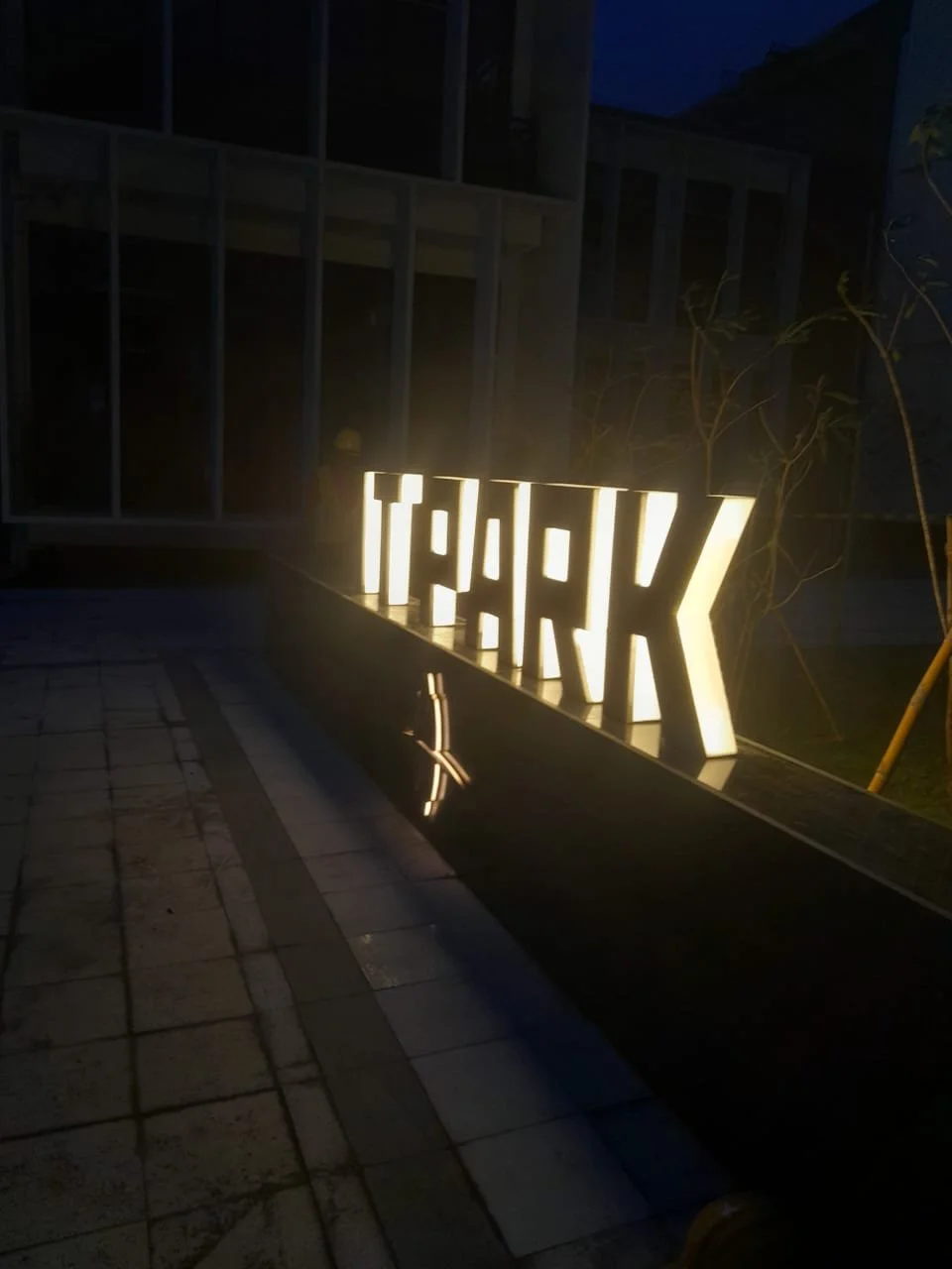 Illuminated sign spelling 'T-H-A-N-K' at night, with reflections visible on a water feature or reflective surface below.