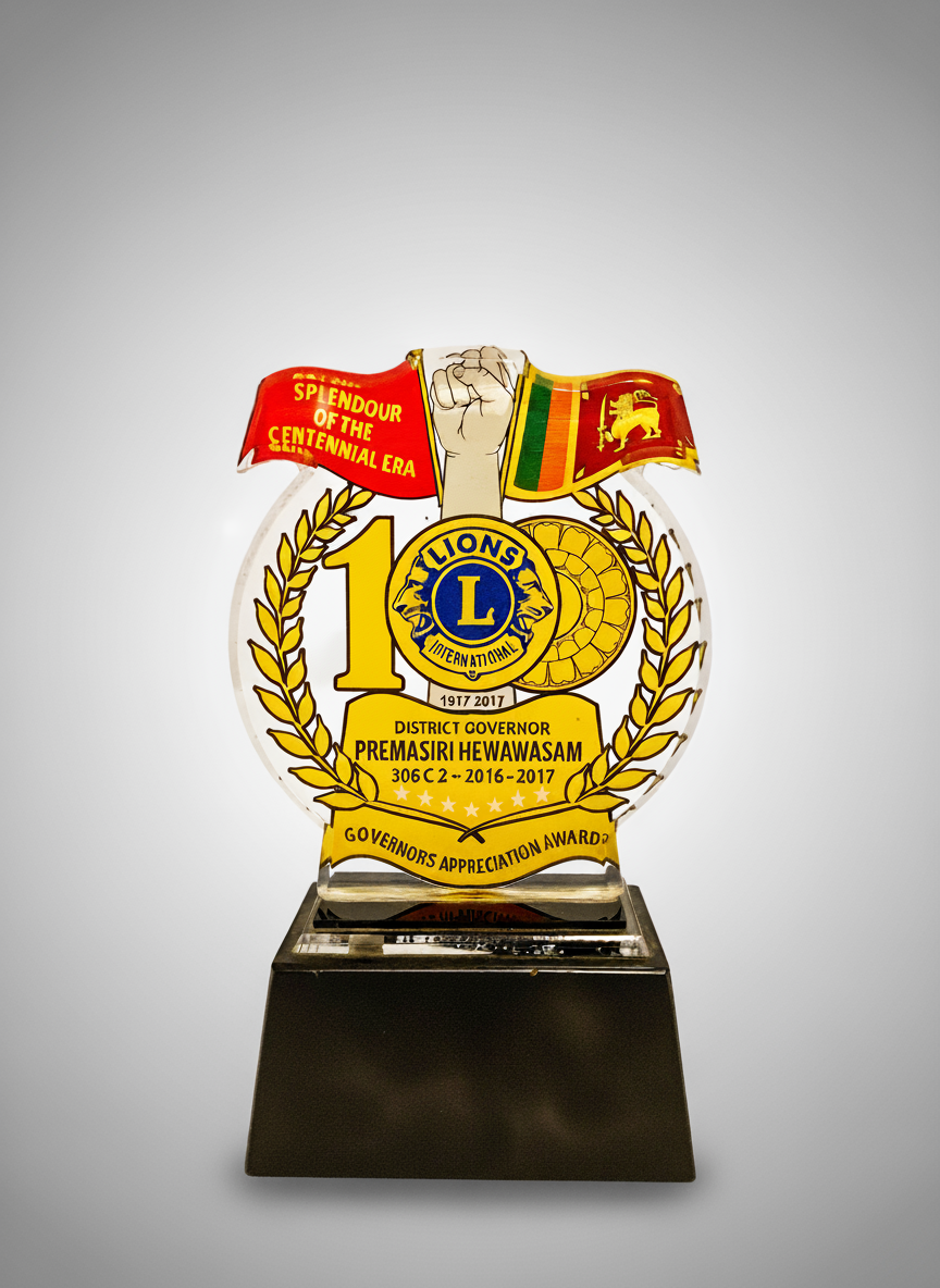 A decorative award with the Lions Club logo, featuring a red and a Sri Lankan flag, a raised fist, and gold laurel leaves, celebrating 100 years from 1917 to 2017 for district governor Premasiri Hewawasam.