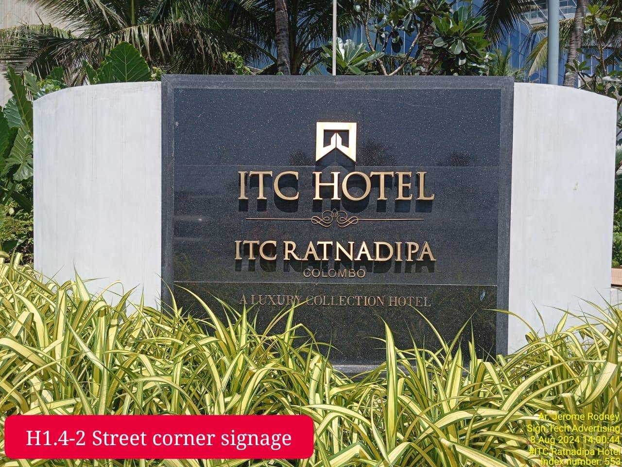 Black hotel sign with gold lettering for ITC RatnadiPA Colombo, surrounded by green plants and trees, indicating it's a luxury hotel.