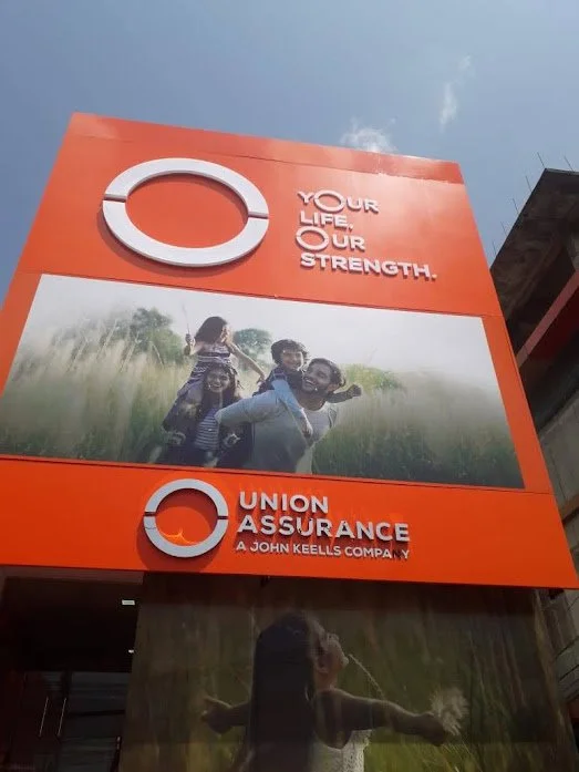 Large orange billboard for Union Assurance with the company's logo, slogan "Your life, our strength," and a photo of a happy family outdoors.