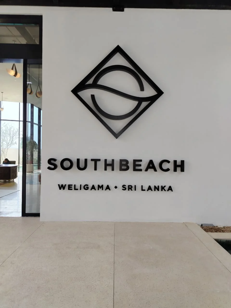 Sign for South Beach Weligama, Sri Lanka, with a modern logo and black lettering on a white wall.