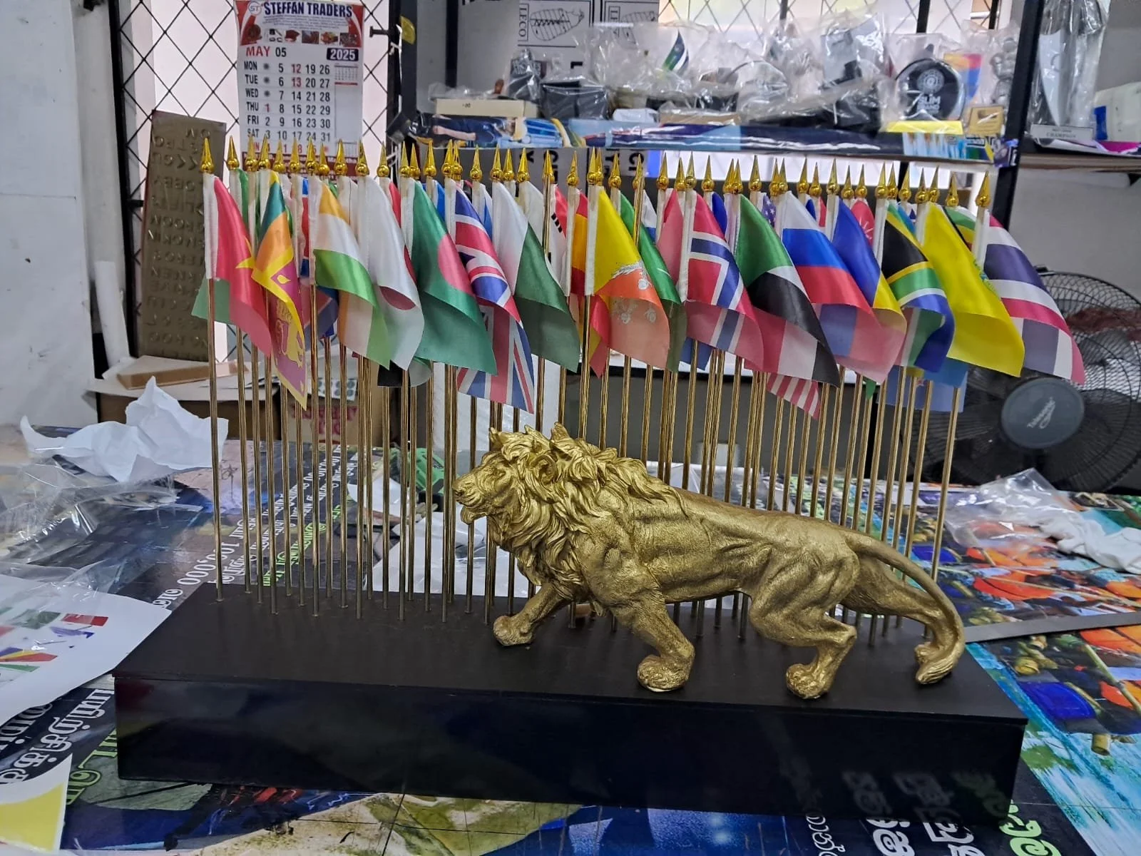 A display of small international flags on golden poles, with a golden lion sculpture in front, all set on a black base.