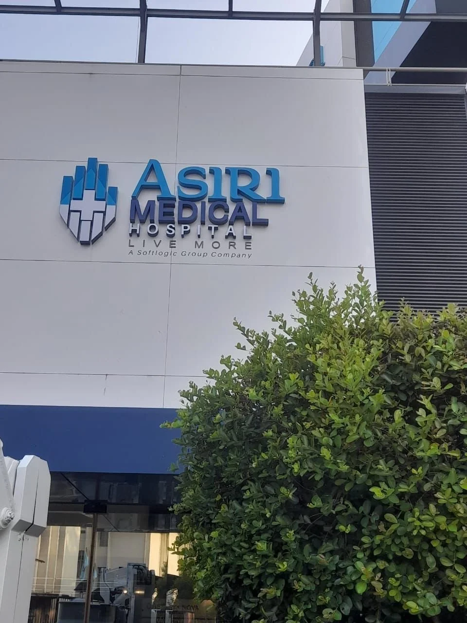 Sign for ASIRI Medical Hospital on a modern building with greenery in front and glass windows above.
