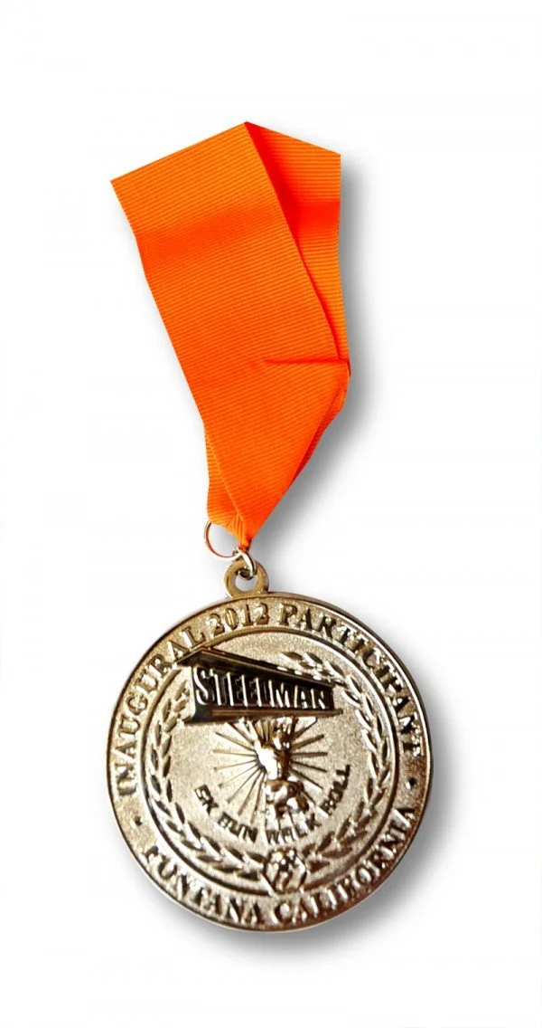 Medal with an orange ribbon, commemorating a 2012 Thanksgiving event, showing a cartoon reindeer and a sign with the word "Sleighman."