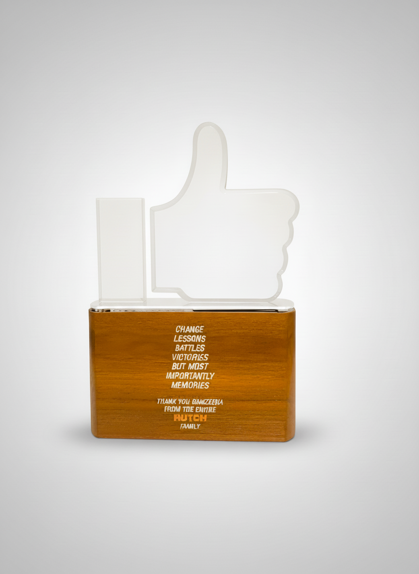 A wooden block with a glass or acrylic 'thumbs up' sign on top, and a message printed on the block about change, lessons, battles, victories, memories, and family.