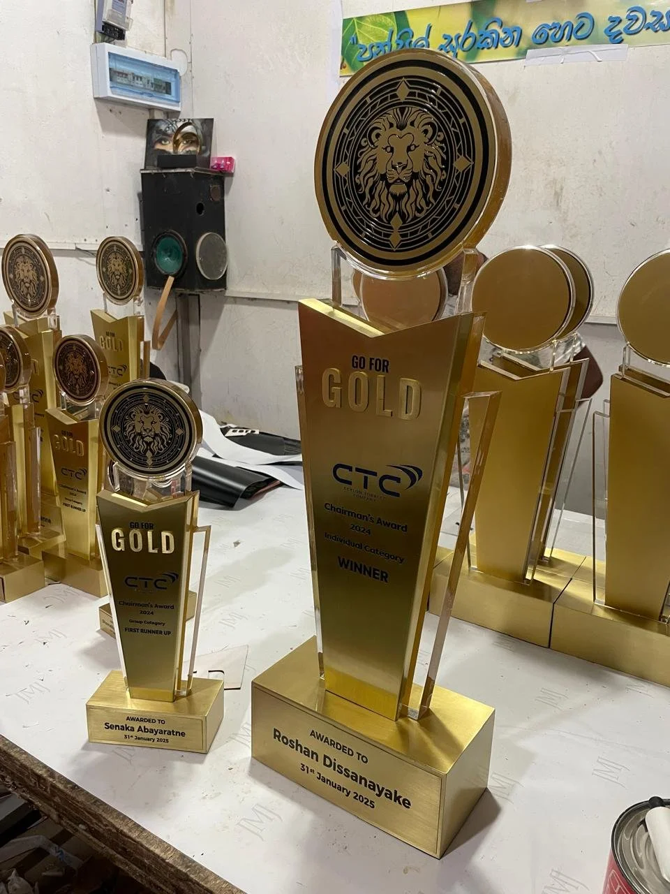 Several golden trophies for a corporate awards event, including one for Group Category Winner and another for Individual Category Winner, with the names Senaka Abayaratne and Roshan Dissanayake, awarded on January 31, 2025.