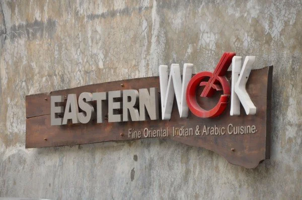 Sign for Eastern WOK restaurant with message about fine oriental, Indian, and Arabic cuisine, mounted on a textured wall.