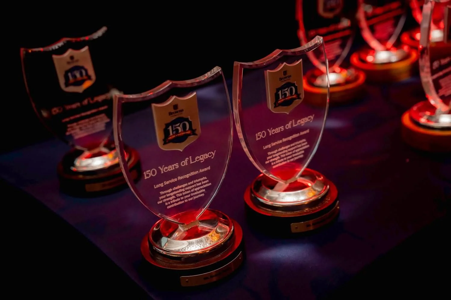 Clear glass awards with black and gold bases and a gold and black emblem on top, arranged on a dark blue tablecloth.