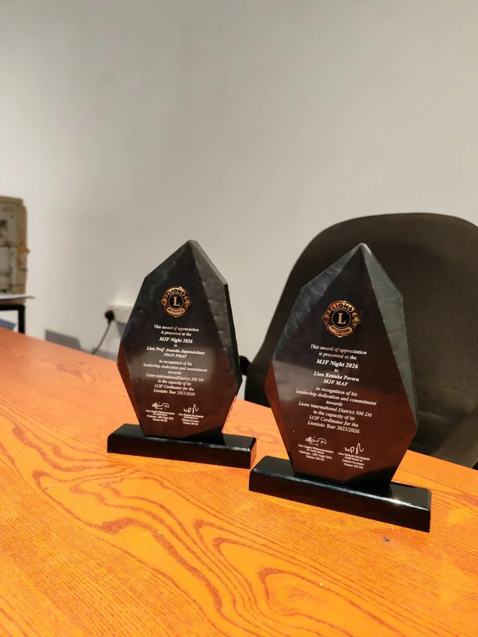 Two black trophies with gold and red Lions Club International logo on top, placed on a wooden table.