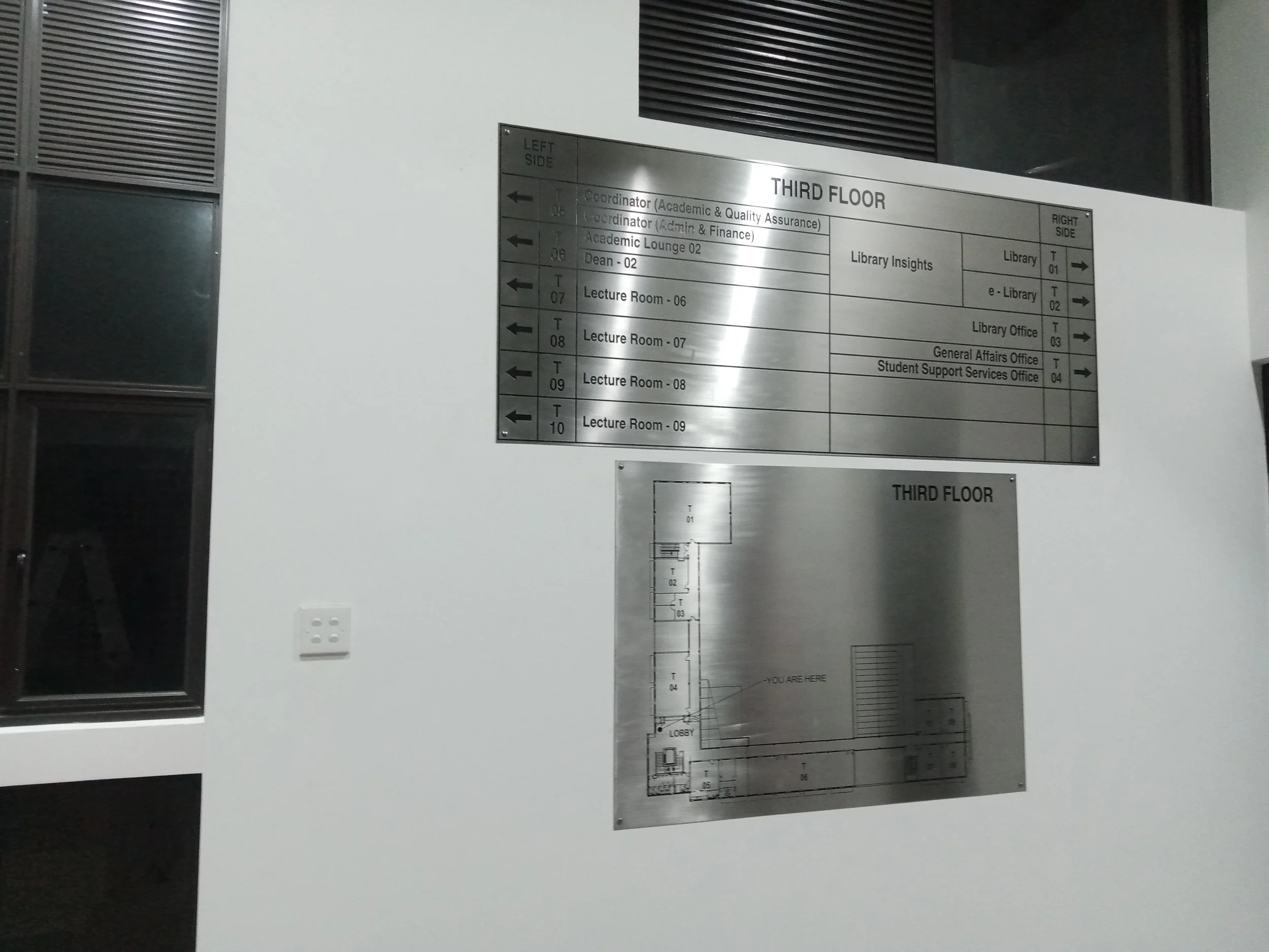 A lobby directory sign on a white wall in a building, displaying floor and room information for the third floor.