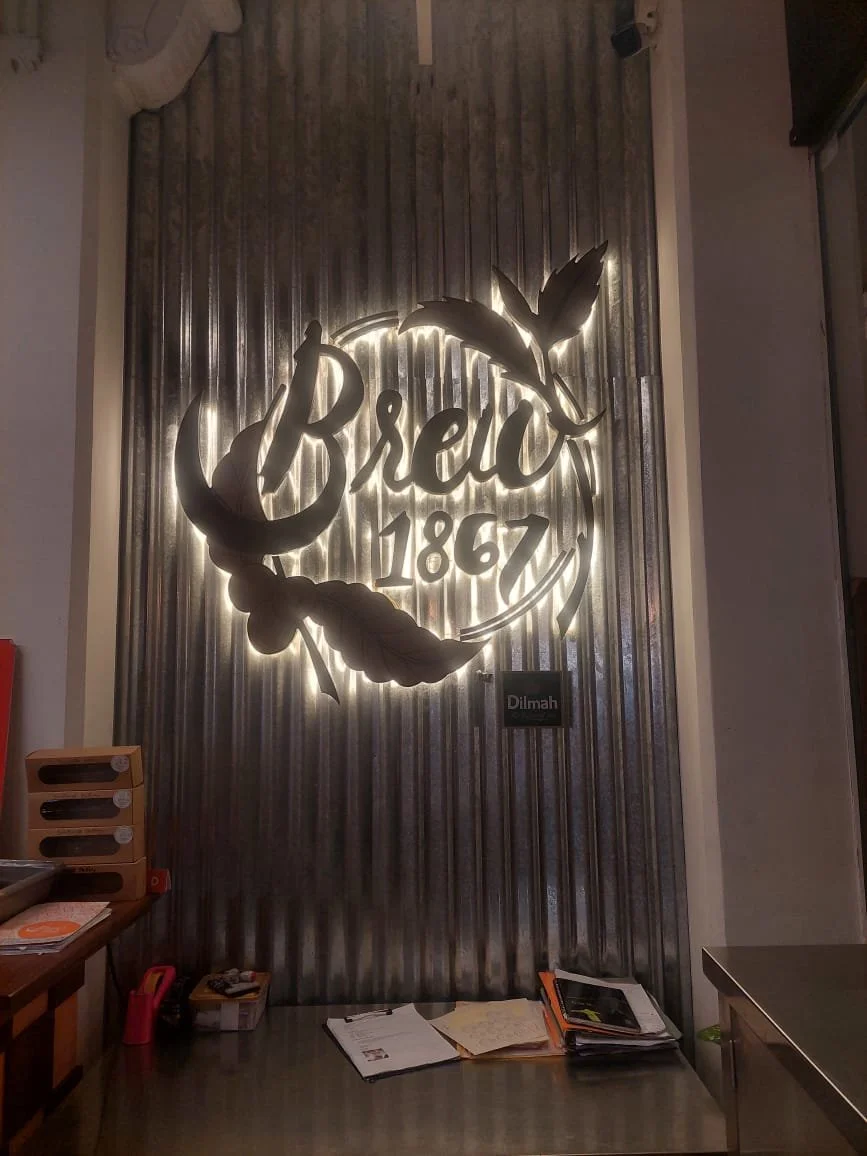 Illuminated metal wall art displaying the word 'Breo', the year '1867', and a feather design in a modern interior space.