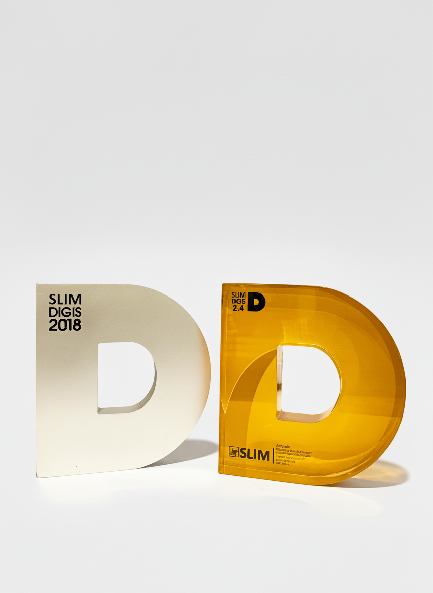 Two large letter D-shaped objects, one matte white and the other translucent yellow, are placed side by side on a plain white surface. The objects are hollow with a cutout in the center, and have text printed on them related to the Slim Digis 2018 ev