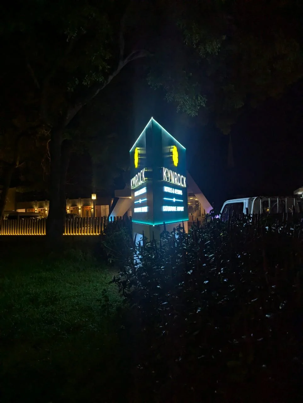 Neon-lit sign for Skyrock music venue at night, surrounded by trees and bushes.